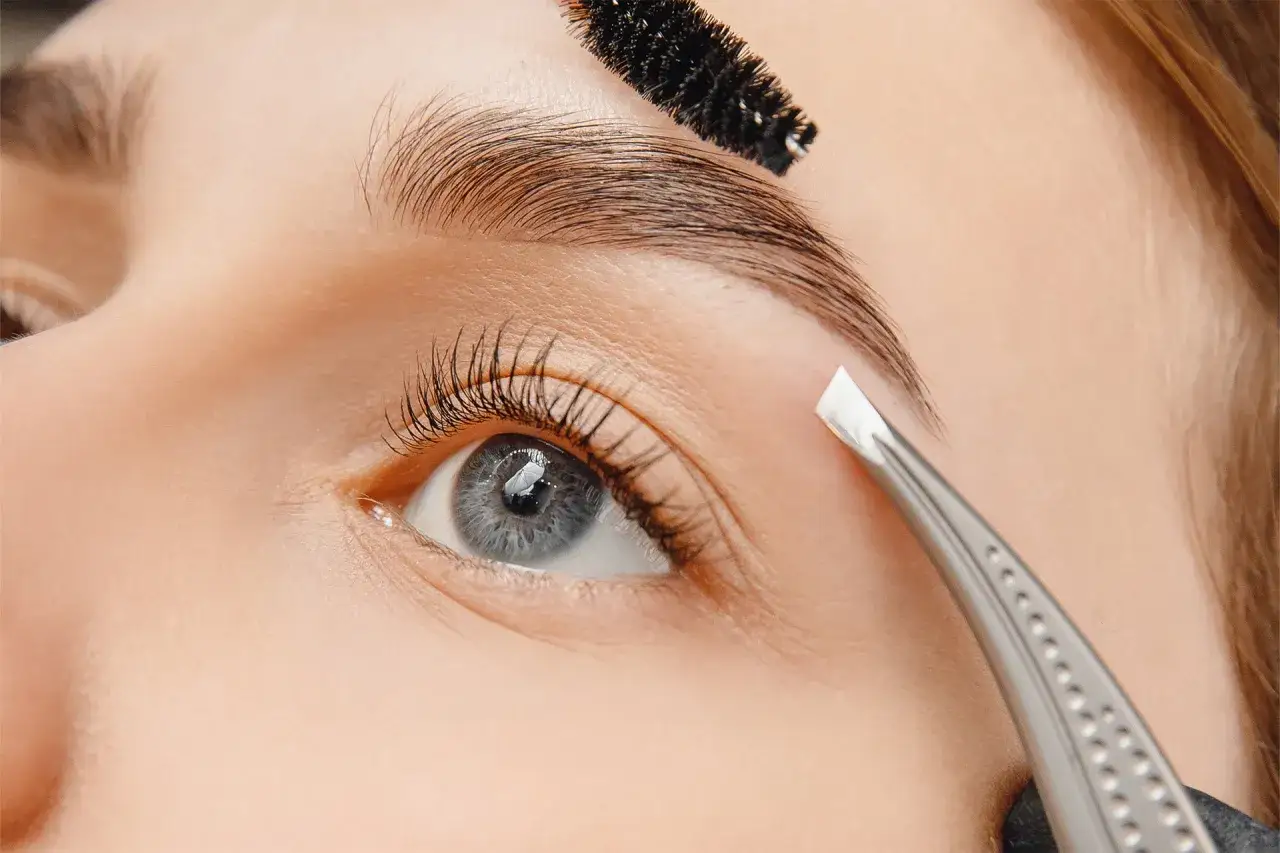 Une pince à épiler est utilisée pour épiler les sourcils d'une femme, créant une forme parfaite.