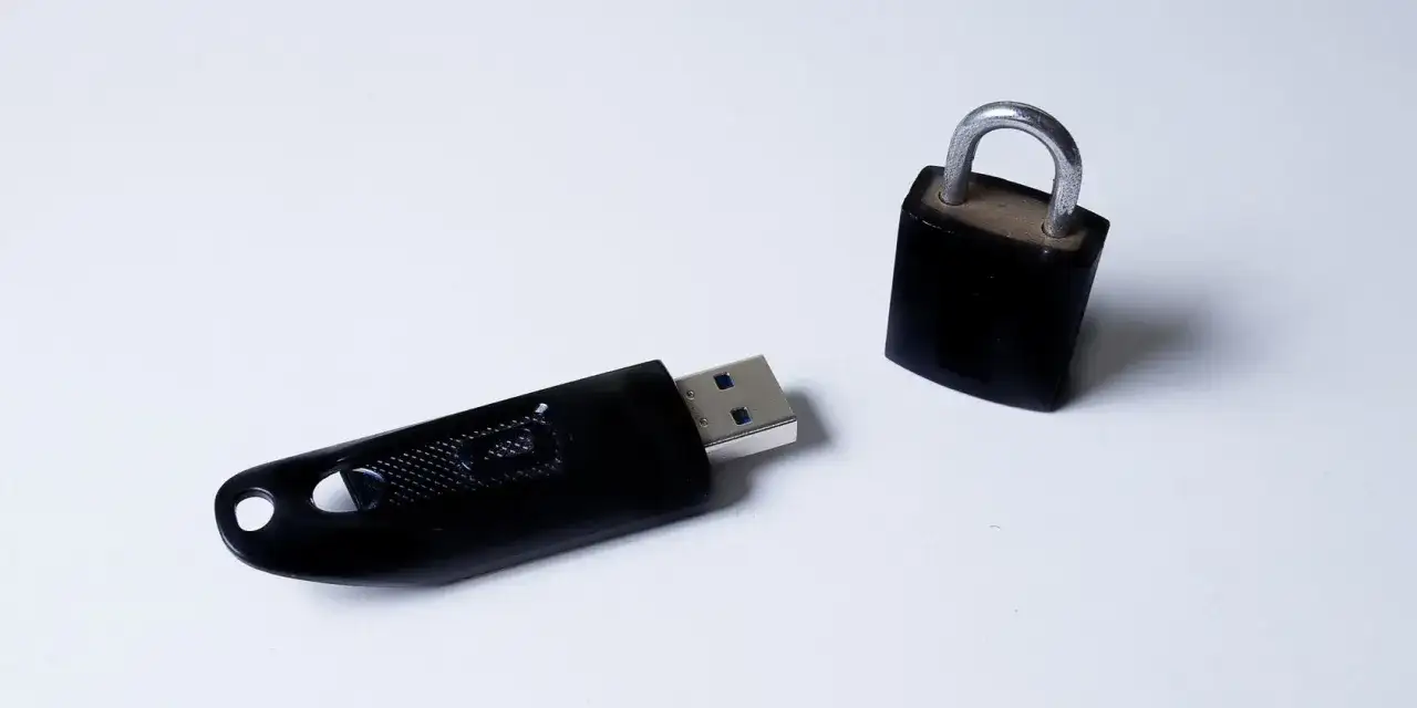 Czarny pendrive leży obok zamkniętej kłódki. Dysk jest zabezpieczony przed zapisem, chroniąc dane.