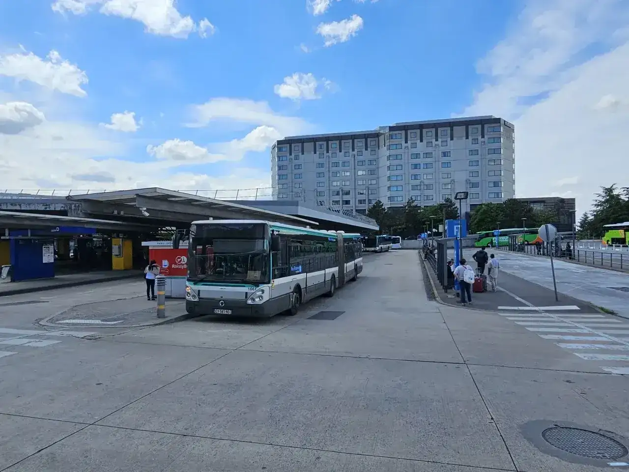 Autobusy na przystanku przy jednym z lotnisk w Paryżu. W tle hotel i inne pojazdy.
