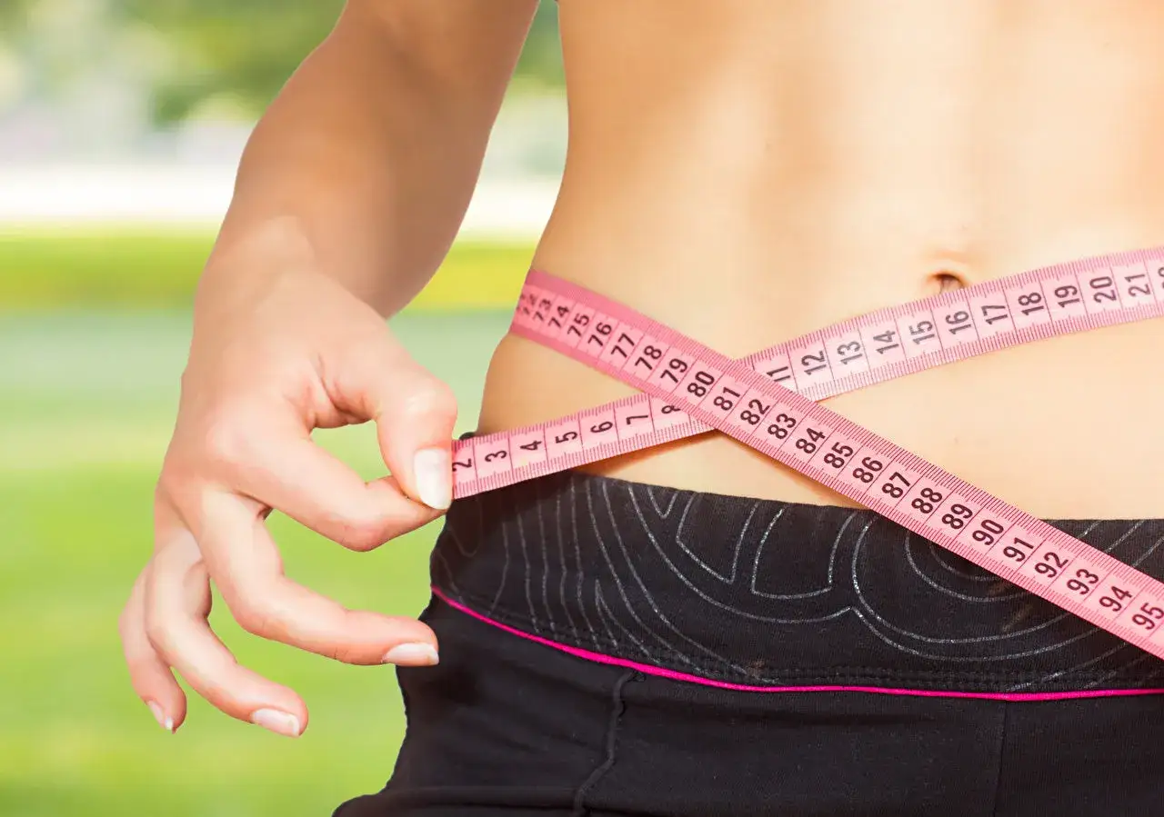 Une femme mesure sa taille avec un mètre ruban rose, se demandant pourquoi je grossis alors que je fais attention.