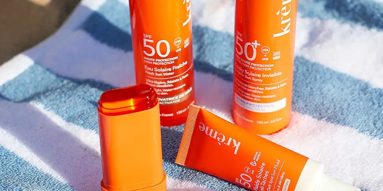 Trois produits de cr&egrave;me solaire uva uvb, dont un stick, sont pos&eacute;s sur une serviette ray&eacute;e. Protection SPF 50.