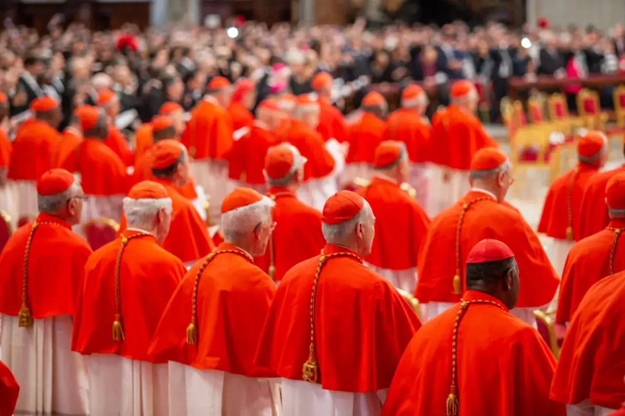 Kardynałowie w czerwonych szatach i piuskach, zgromadzeni na ważnym wydarzeniu, być może konsystorz.