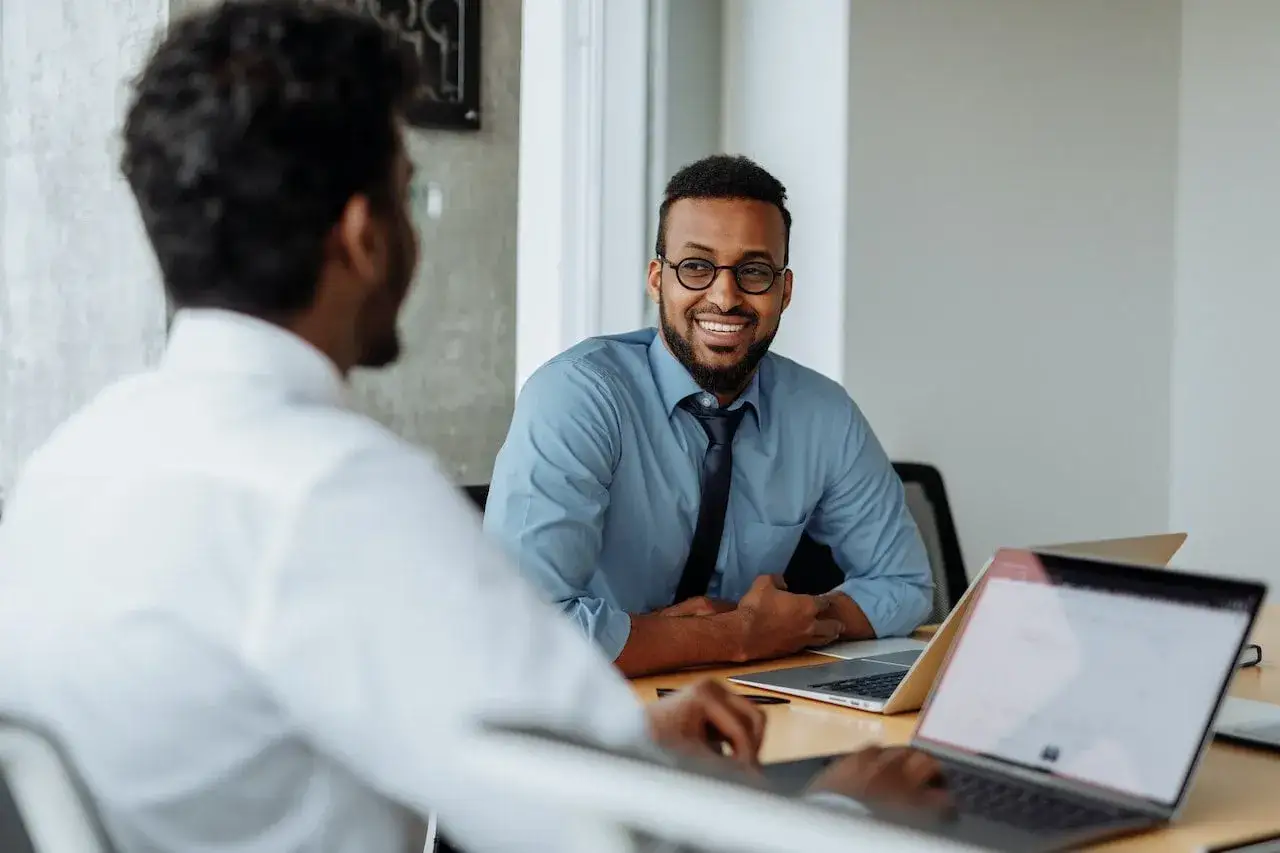Two men in a meeting, one smiling, discussing mid year review examples.