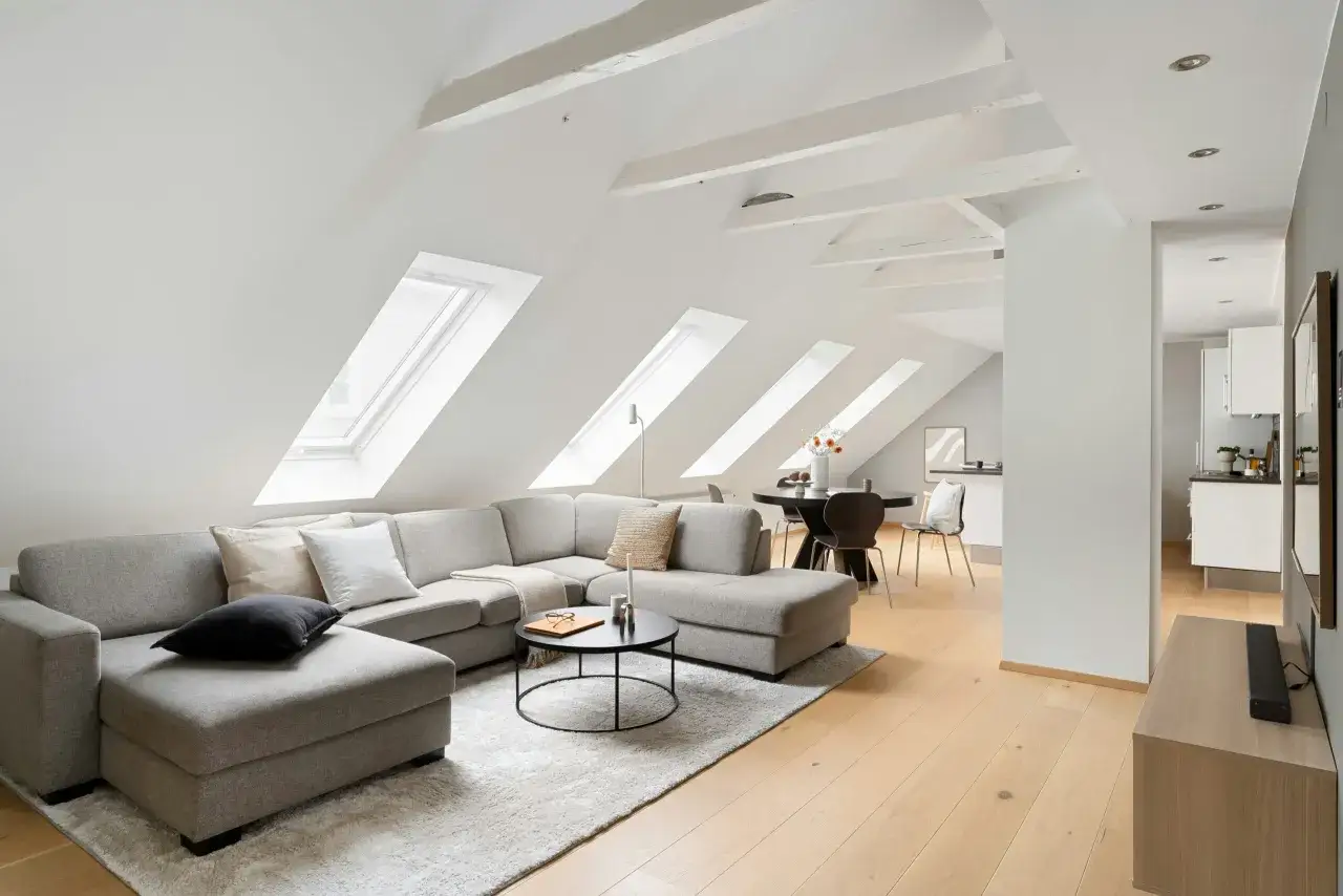 Accogliente salotto in mansarda con divano angolare grigio, tavolino nero e lucernari sul soffitto inclinato.