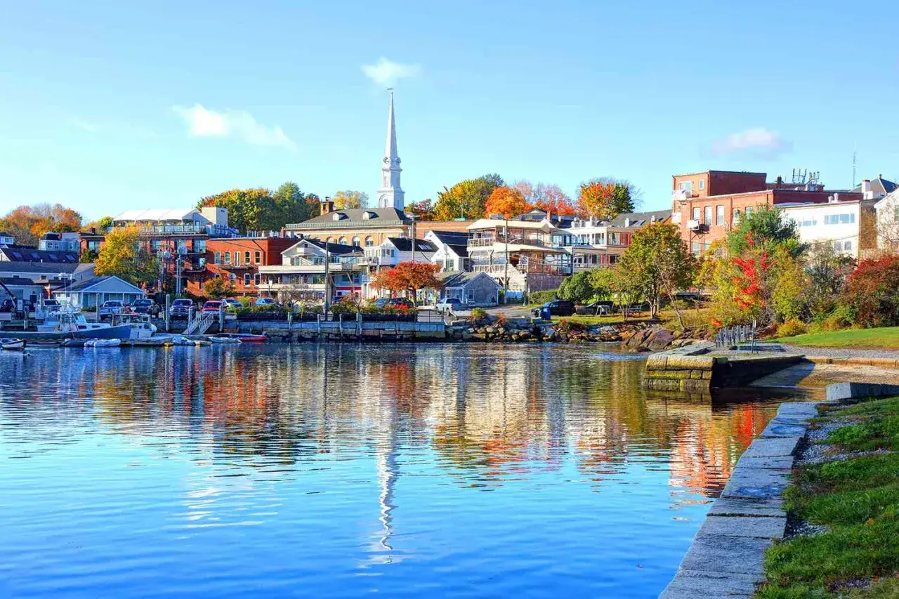 A picturesque harbor town in New England, perfect for weekend getaways. Boats bob on the water, reflecting colorful autumn foliage and charming buildings.