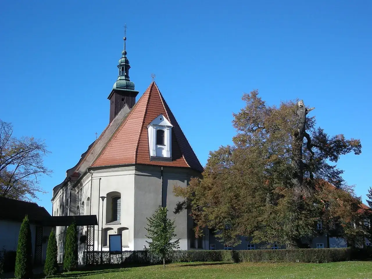 Kościół z wieżą i drzewem, miejsce związane z objawieniami maryjnymi w Polsce.