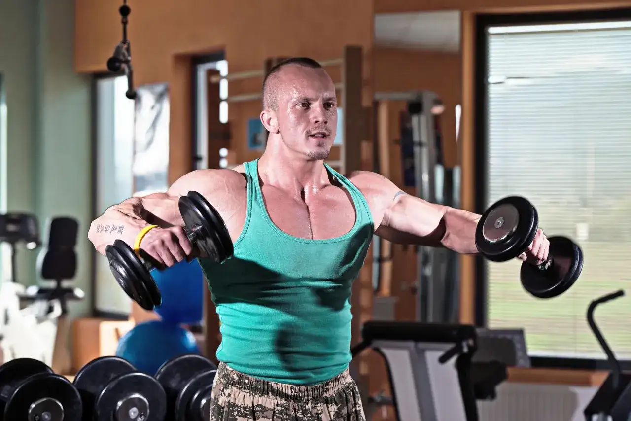Man utf&ouml;r lateral raise med hantlar i ett gym.