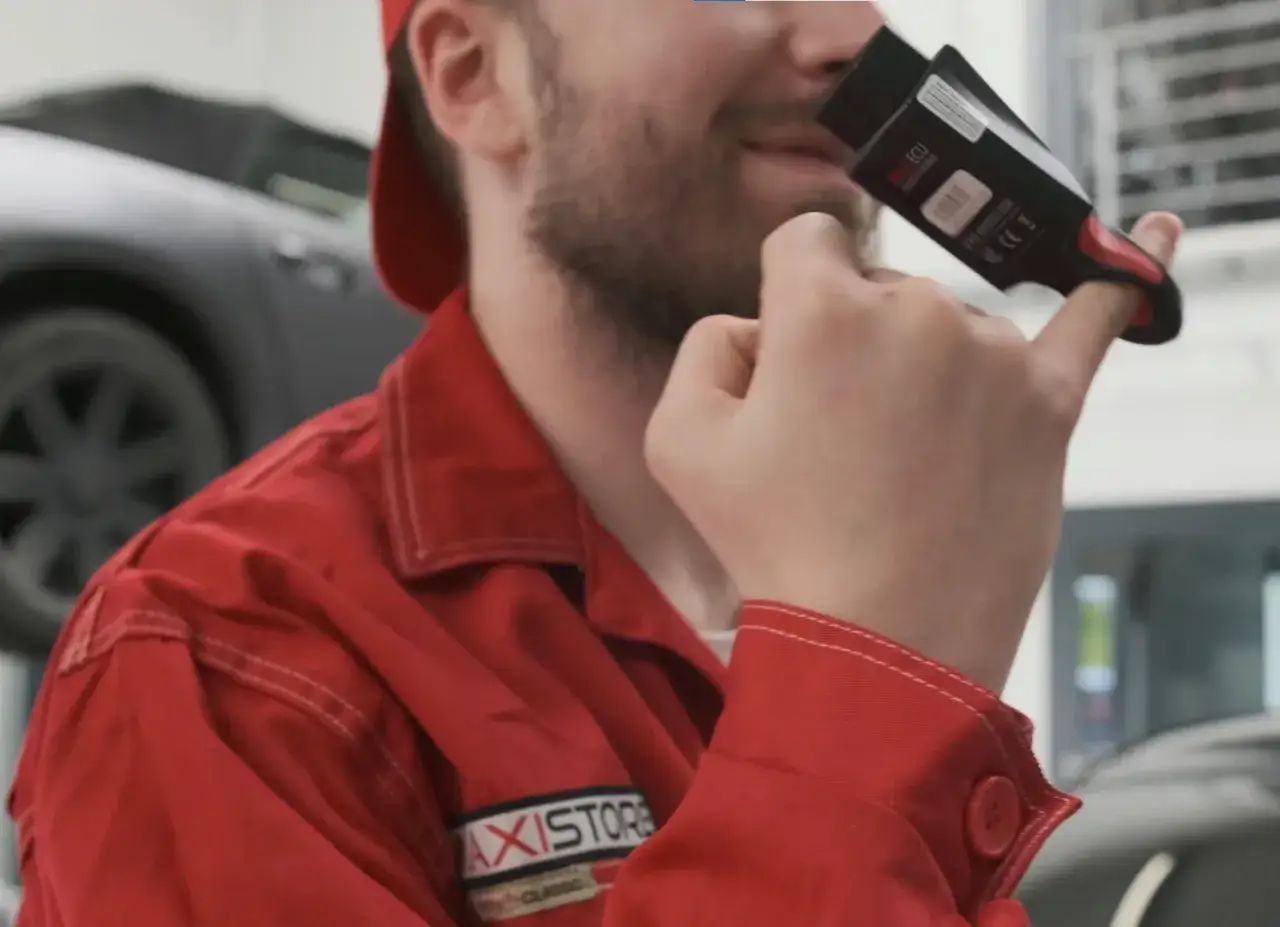 Mechanik w czerwonym kombinezonie analizuje urządzenie diagnostyczne, być może szukając przyczyn **ssangyong korando awarie**.