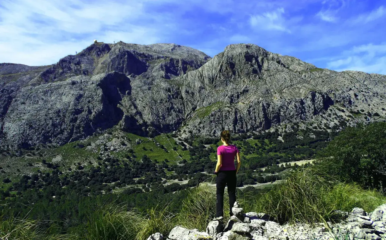 Kobieta podziwia majestatyczne góry Serra de Tramuntana. Idealne miejsce na zimowe wędrówki, by odkryć jakie trasy na Majorce w górach Serra de Tramuntana wybrać zimą.