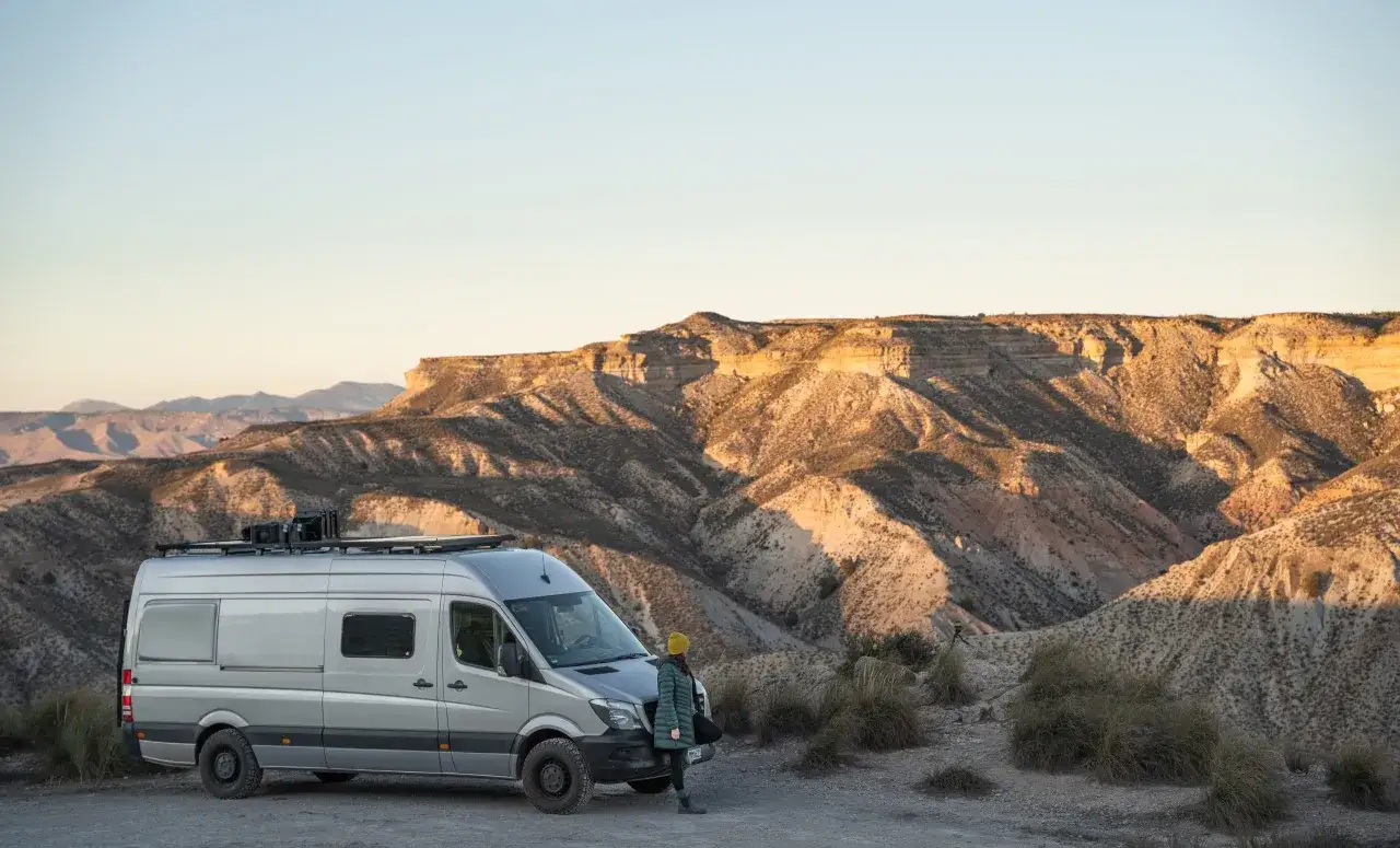 Ein Campervan steht in der W&uuml;ste Spaniens, bereit f&uuml;r wildcampen. Die Sonne beleuchtet die zerkl&uuml;fteten Berge im Hintergrund.