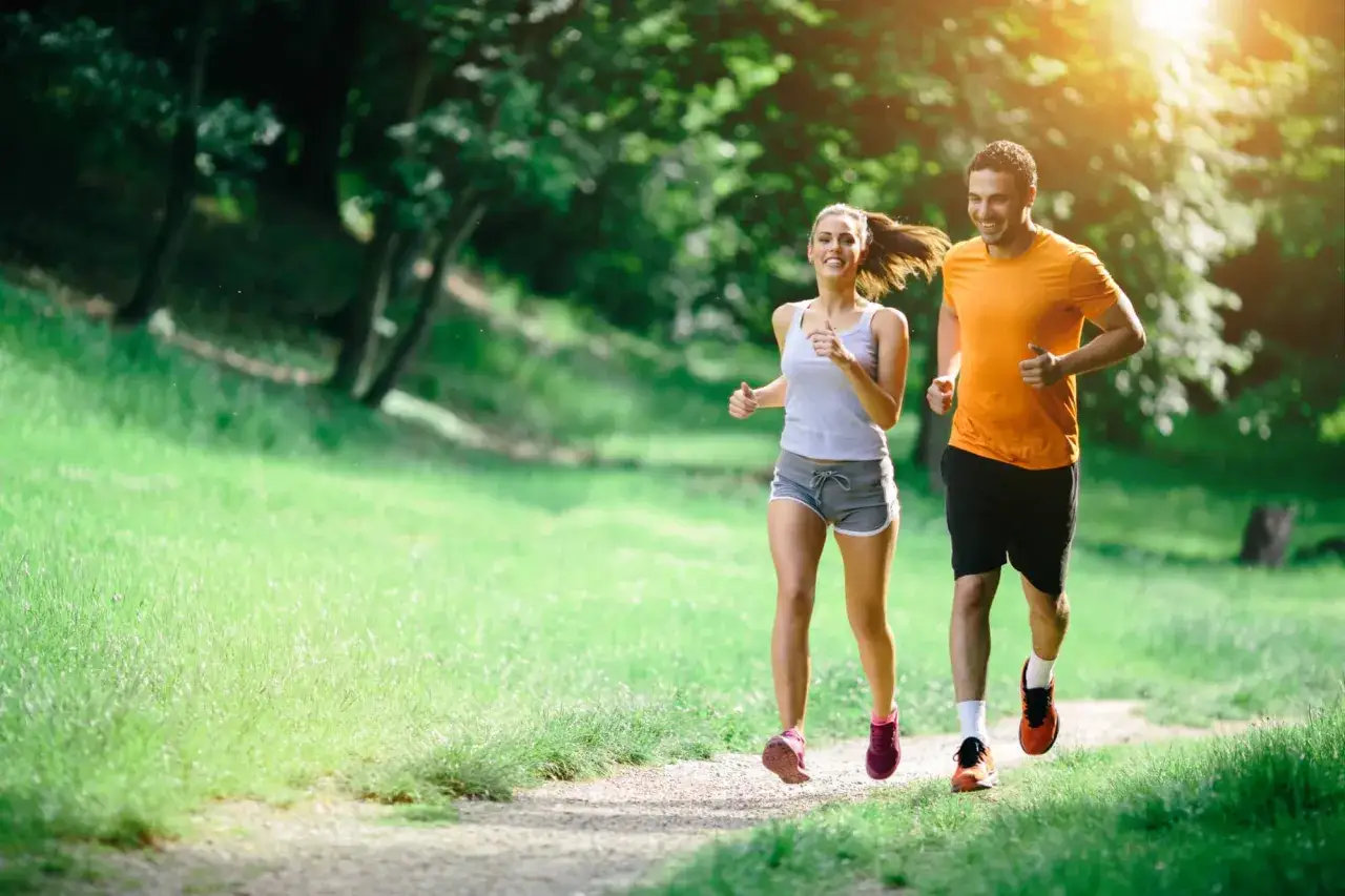 Pareja corriendo en un parque soleado, una forma natural de aumentar la dopamina y sentirse feliz.