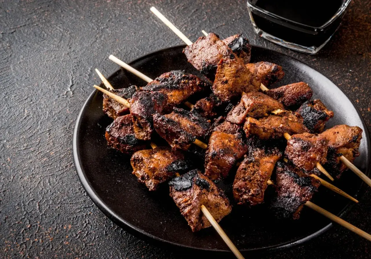 Spiedini di carne succulenti e grigliati, pronti per essere intinti in una salsa scura.