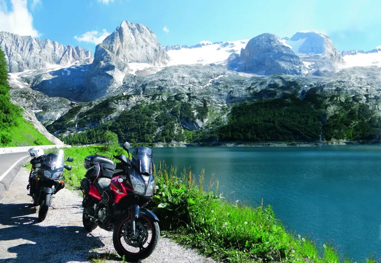 Dwa motocykle zaparkowane nad turkusowym jeziorem, w tle majestatyczne, ośnieżone góry. Idealne miejsce na podróż szwajcaria motocyklem.