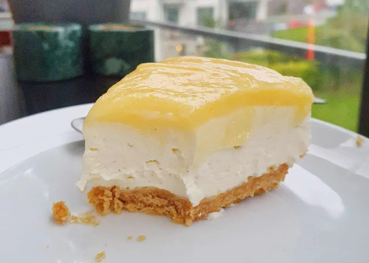En bit krämig citron cheesecake med kexbotten och gul topping. Perfekt för en fika.