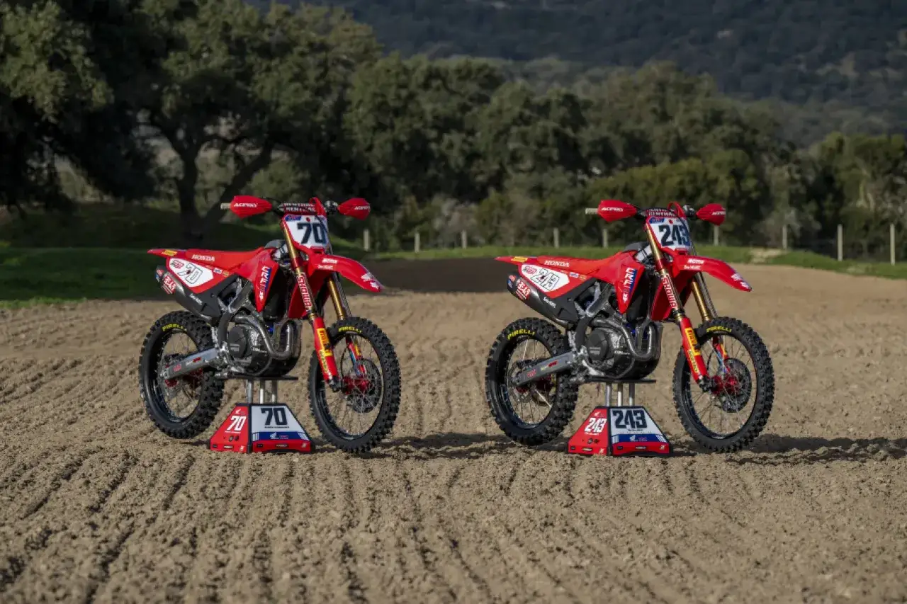 Dos motos Honda CRF 450R rojas listas para la carrera en un circuito de tierra.