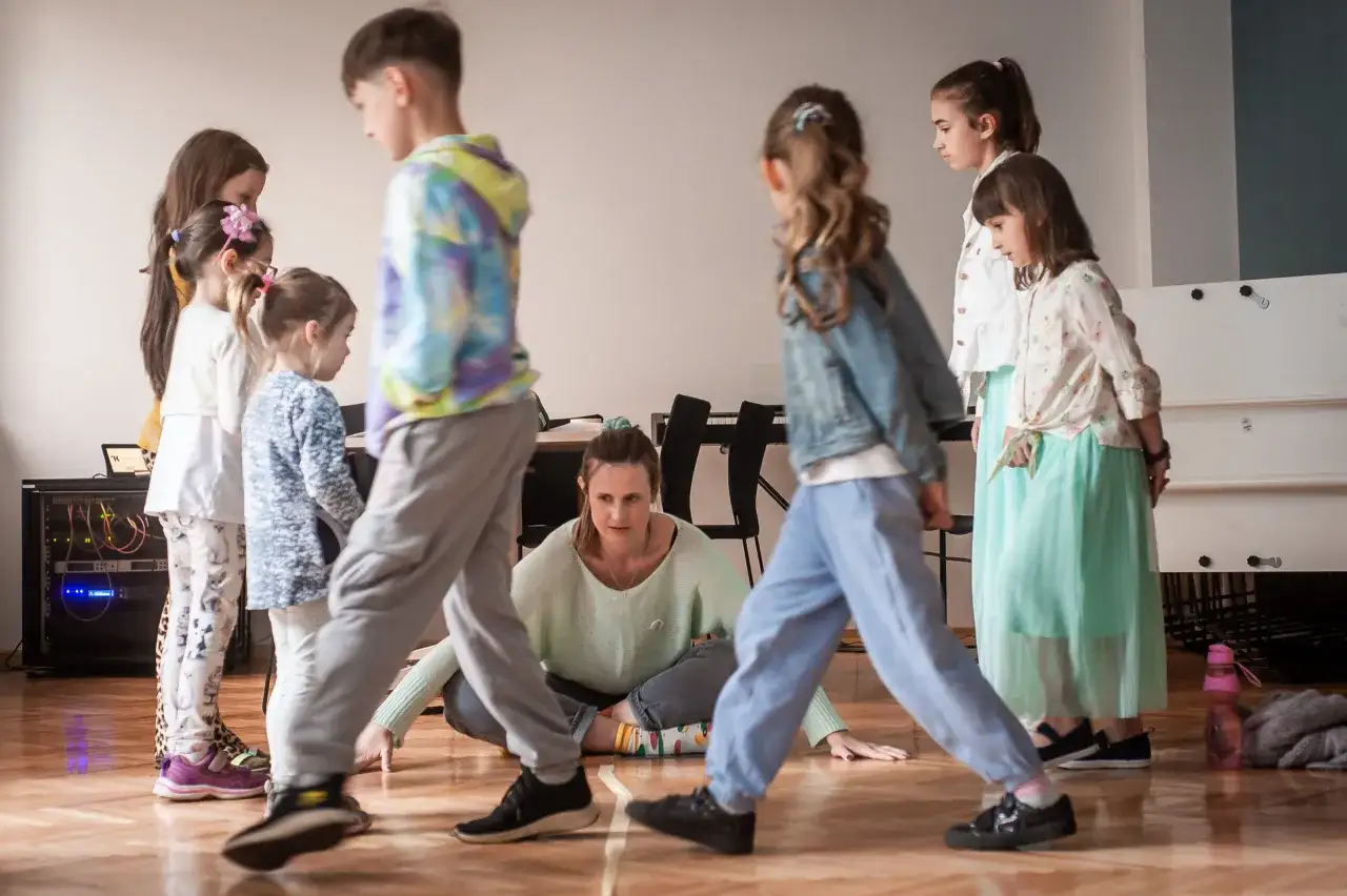 Dzieci i instruktorka ćwiczą ruchy na zajęciach teatralnych dla młodzieży.