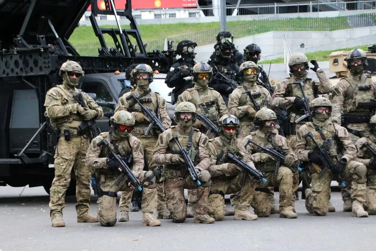 Grupa komandosów w pełnym rynsztunku, gotowa do akcji. W tle pojazd taktyczny.