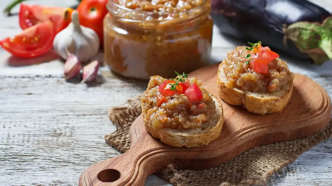 Deux toasts garnis de le vrai caviar d'aubergine, garni de tomates fra&icirc;ches et d'une touche de thym, sur une planche en bois.
