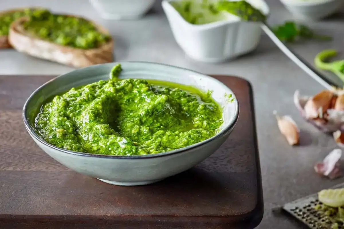 Pesto z bazylii w misce, idealne do przechowywania na zimę. Obok czosnek i grzanki.