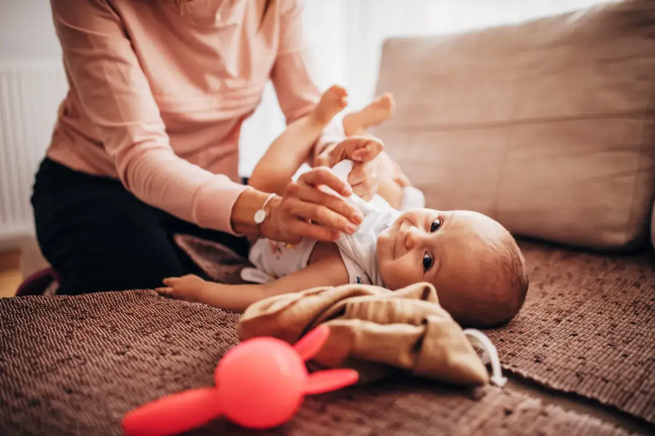 Mama troszczy się o maluszka, nawet kiedy kryzys laktacyjny daje się we znaki. Uśmiechnięte dziecko na kanapie.