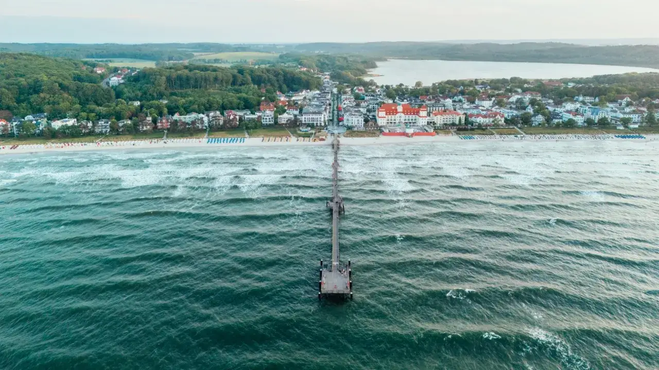 Die Seebr&uuml;cke Binz erstreckt sich ins Meer, mit dem Strand und der Kurkarte Binz im Hintergrund.