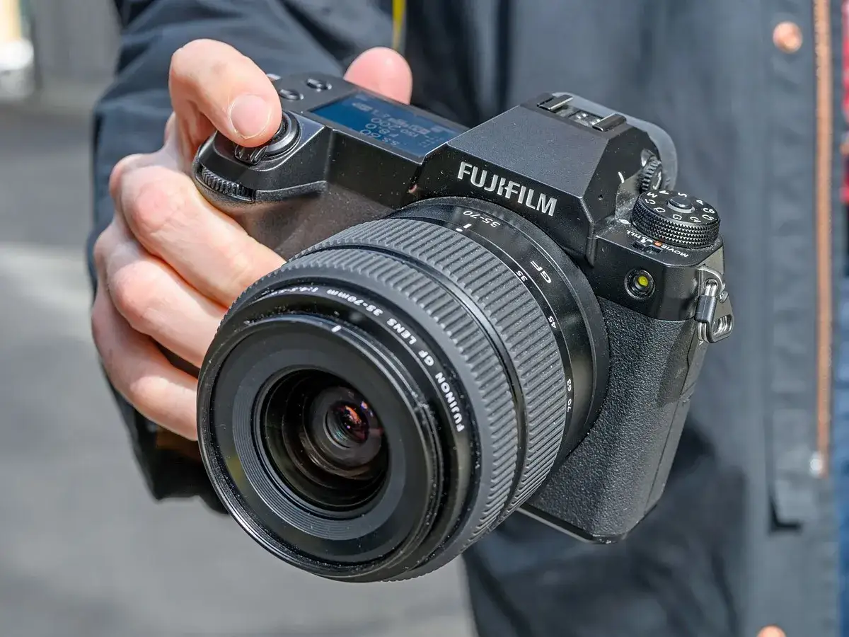 En hand h&aring;ller en Fujifilm GFX 50S II med ett GF 35-70mm objektiv.