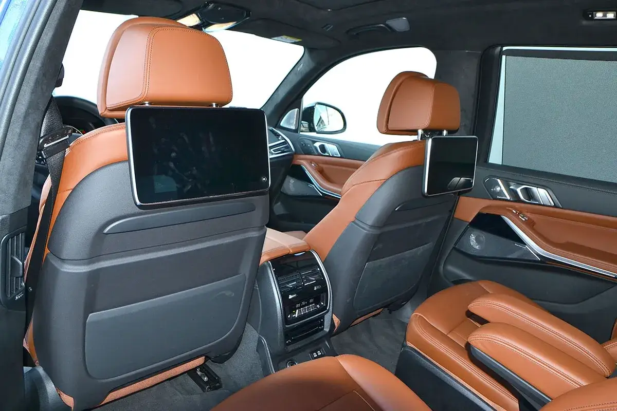 Wnętrze BMW X7 2025 z brązową skórzaną tapicerką i ekranami multimedialnymi dla pasażerów z tyłu.