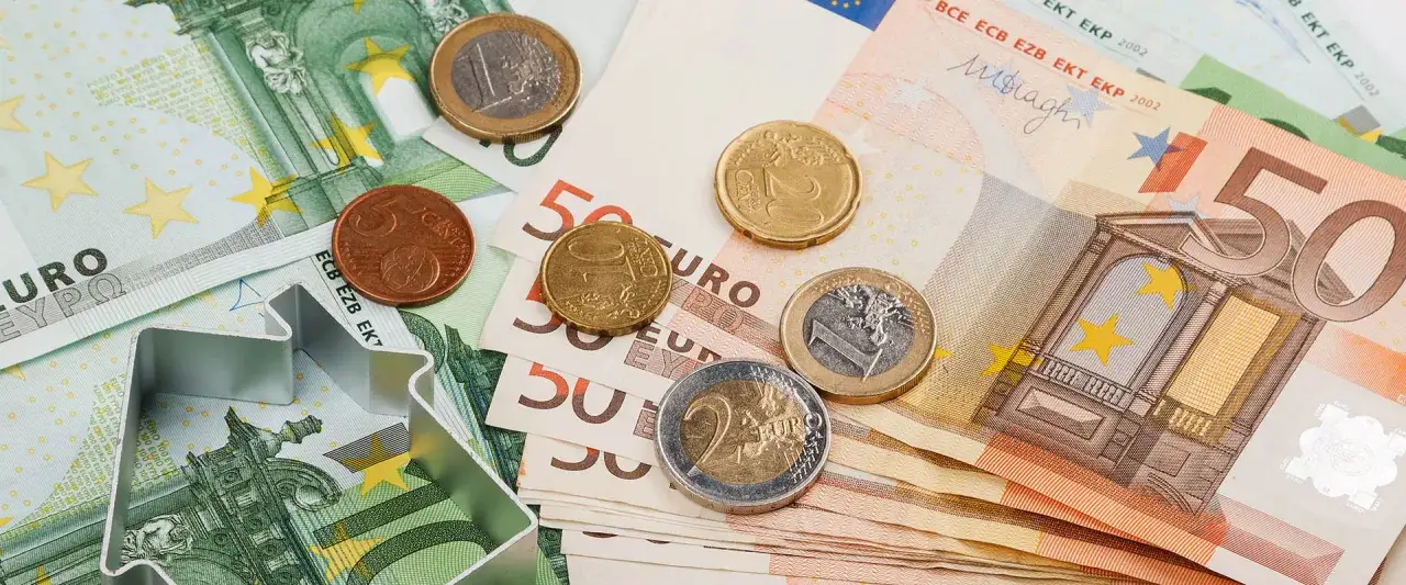 Euro banknoty i monety, czyli waluta we Włoszech. Metalowa forma do ciastek w kształcie domu leży na pieniądzach.