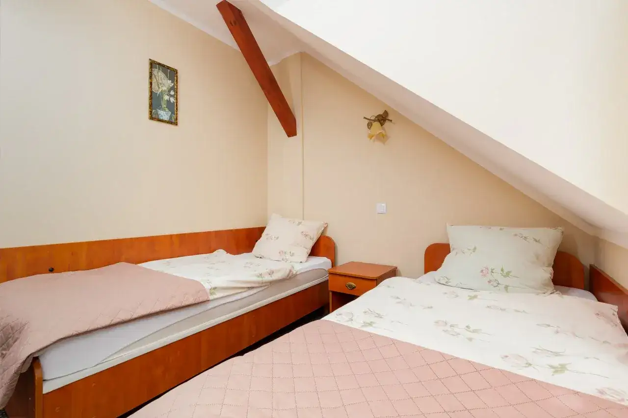 Przytulny pokój z dwoma łóżkami w pensjonacie Piast Rewal. Jasne ściany, drewniane meble i pastelowa pościel tworzą miłą atmosferę.