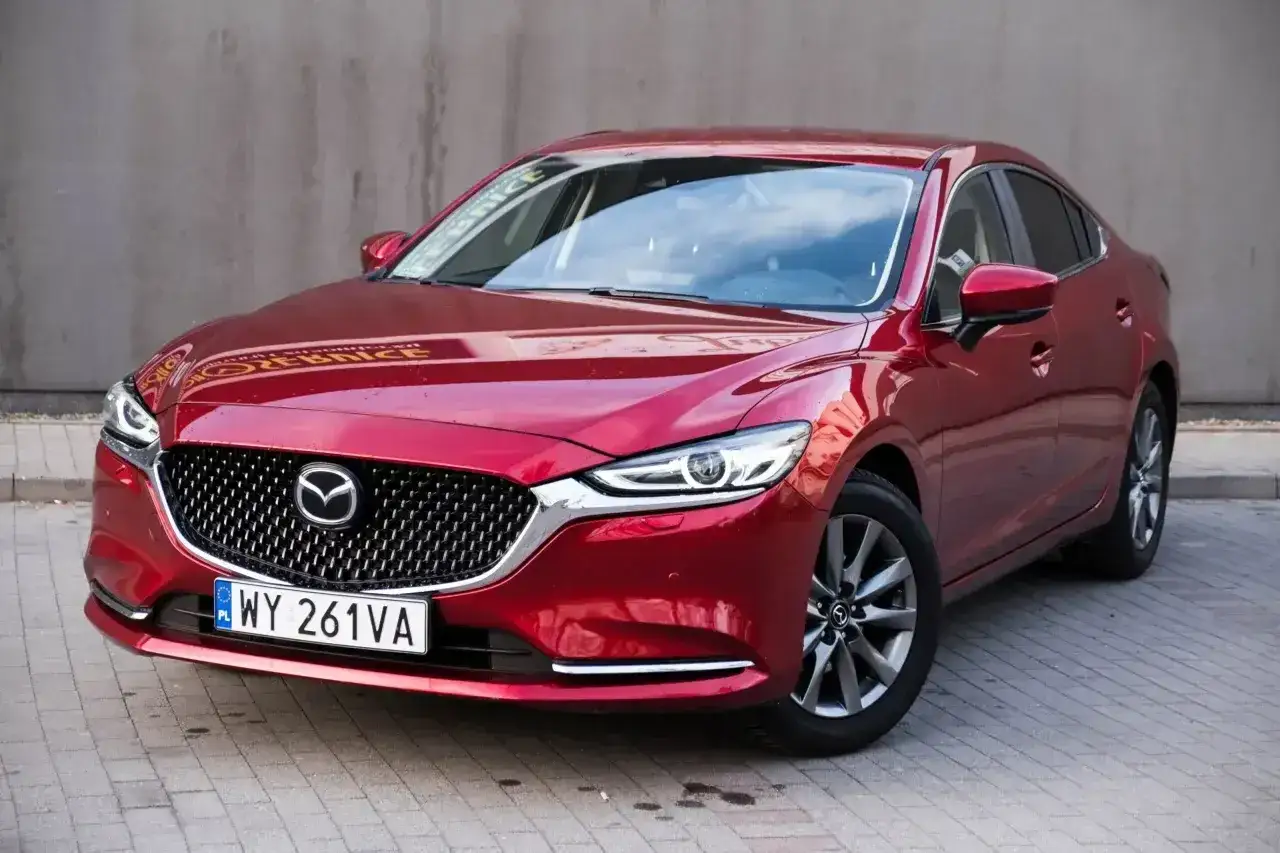 Czerwona Mazda 6 2.0 benzyna z eleganckim grillem i reflektorami LED, zaparkowana na kostce brukowej.