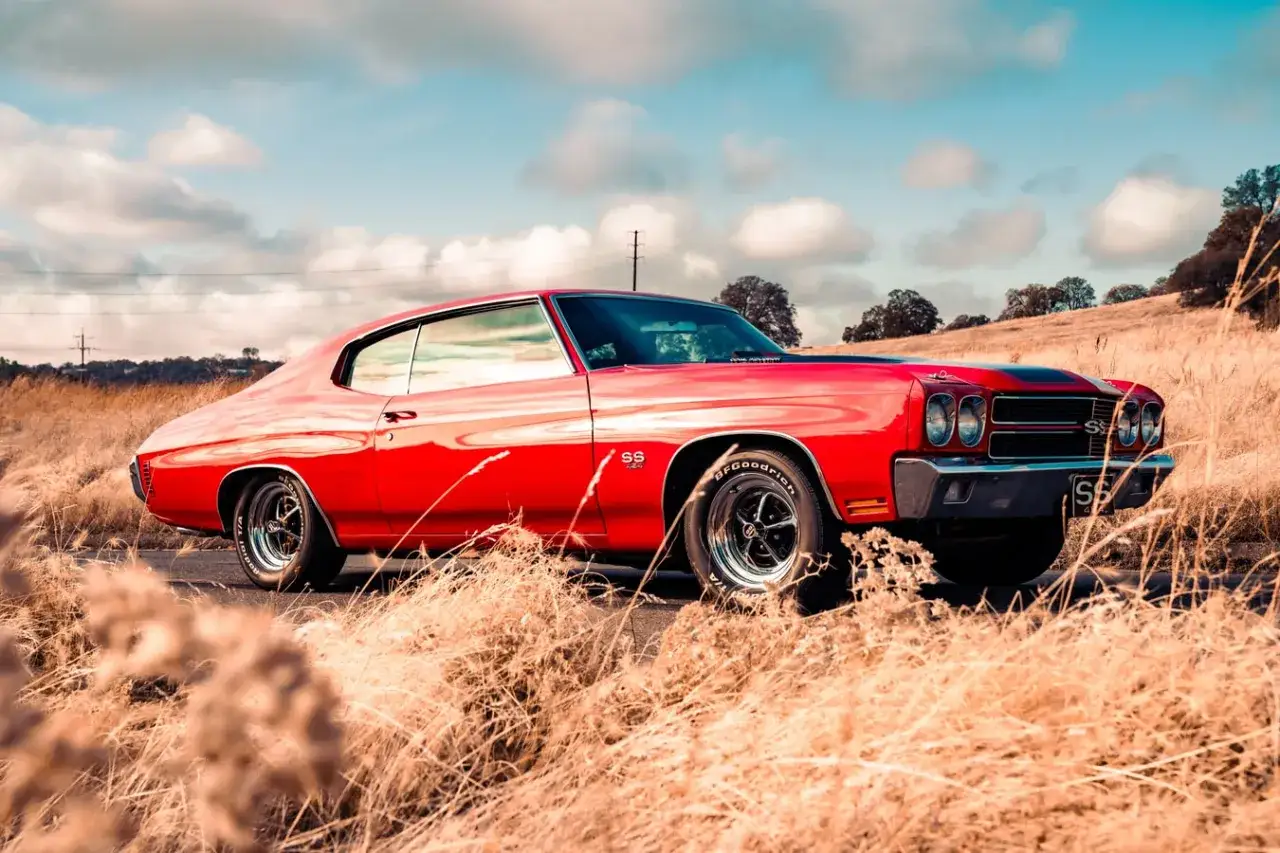R&ouml;d klassisk Chevelle SS, en ikonisk gm bilar, parkerad i torrt gr&auml;s under en molnig himmel.
