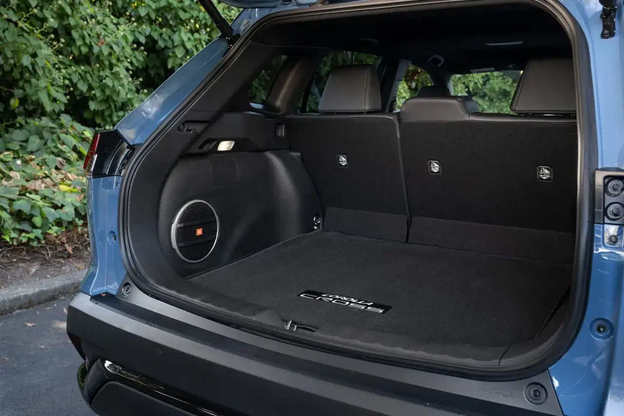 Bagutrymmet i en blå Toyota Corolla Cross testbil, med en JBL-subwoofer och mattor med modellnamnet.