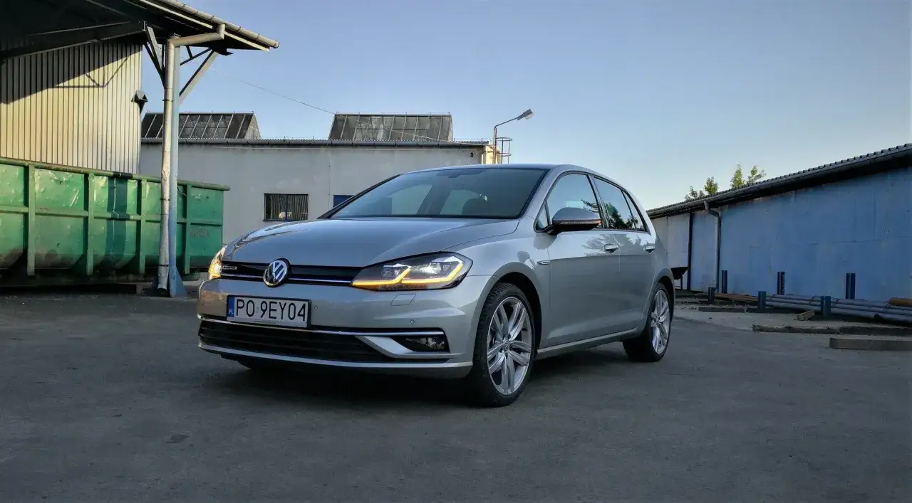 Srebrny Volkswagen Golf z napisem Bluemotion, co oznacza jego ekologiczny charakter, stoi na tle magazynów.