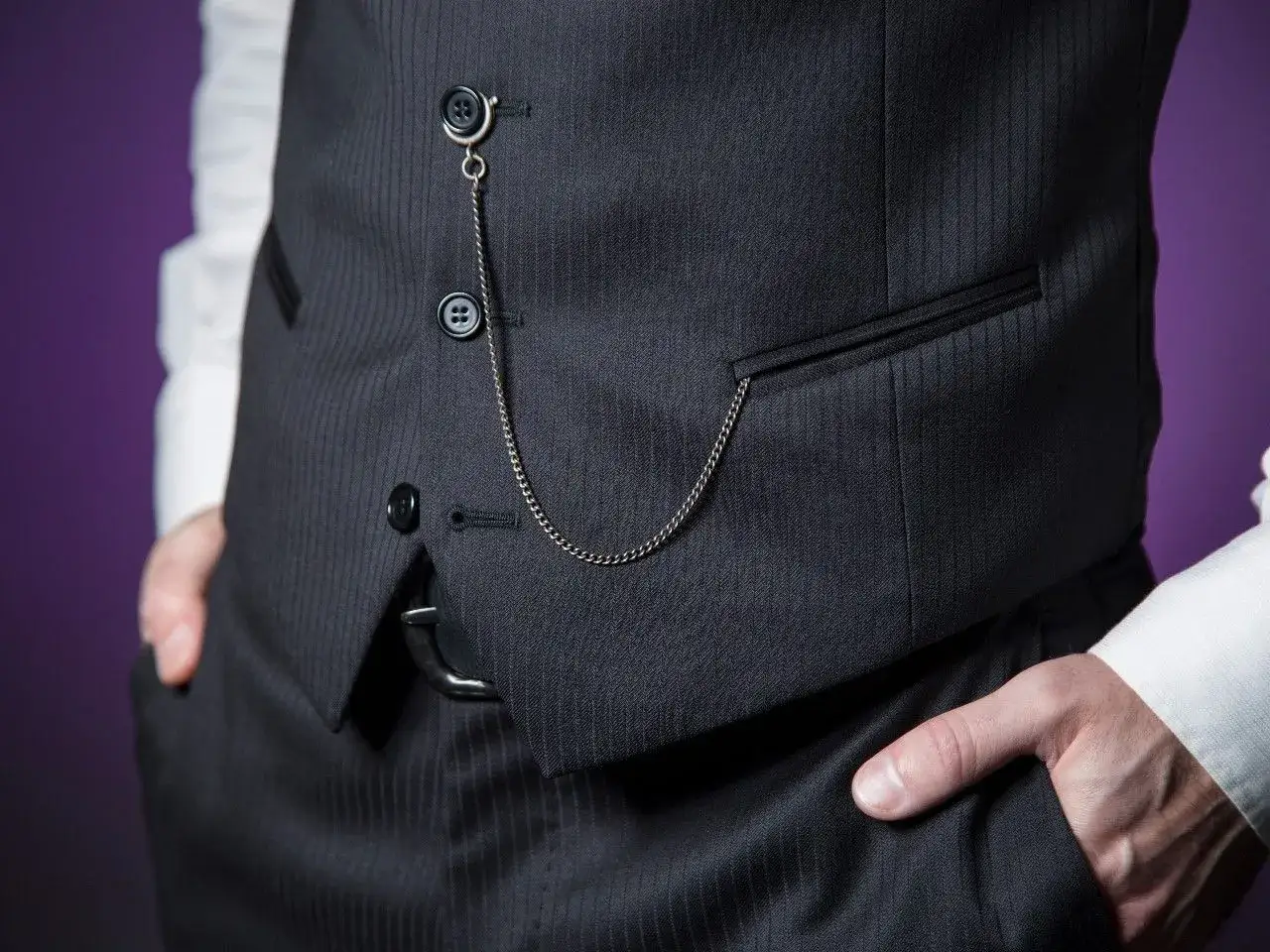 Elegancki str&oacute;j formalny z kamizelką i łańcuszkiem do zegarka kieszonkowego. Dłoń w kieszeni spodni.