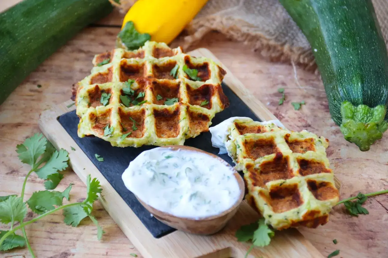 Gaufres de courgette dorées, garnies de persil frais, servies avec une sauce crémeuse. Un délice végétal !