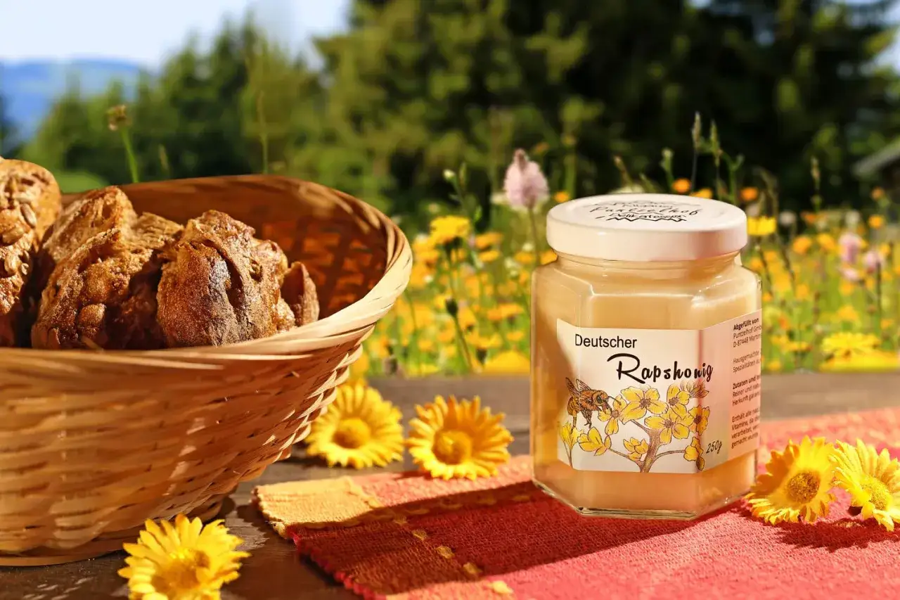 Ein Glas deutscher Raps honig steht neben einem Korb mit Brot. Raps honig gesund und lecker, ein Genuss f&uuml;r jeden Tag.