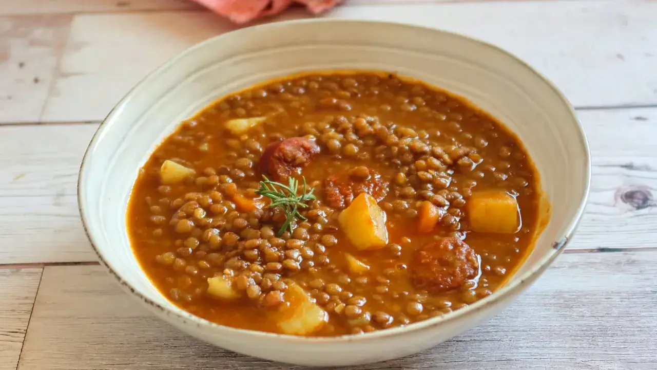 Un taz&oacute;n de lentejas estofadas con trozos de patata y chorizo, decorado con una ramita de romero.