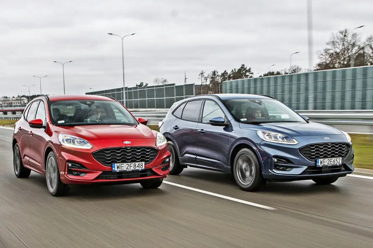 Dwa modele Ford SUV jadące obok siebie po drodze. Czerwony i niebieski Ford Kuga.