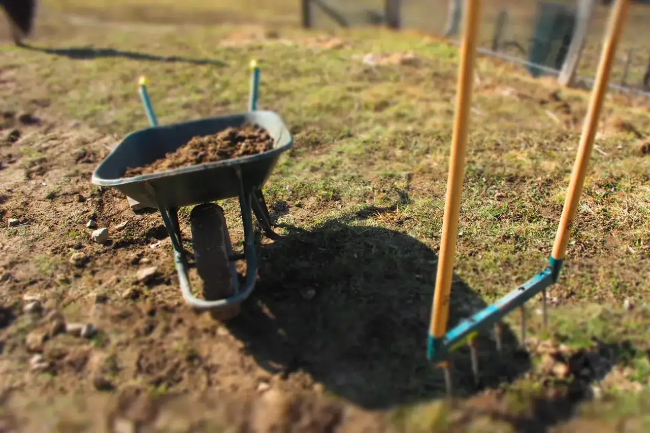 Brouette remplie de terre et râteau prêts à ameublir la terre pour le jardinage printanier.