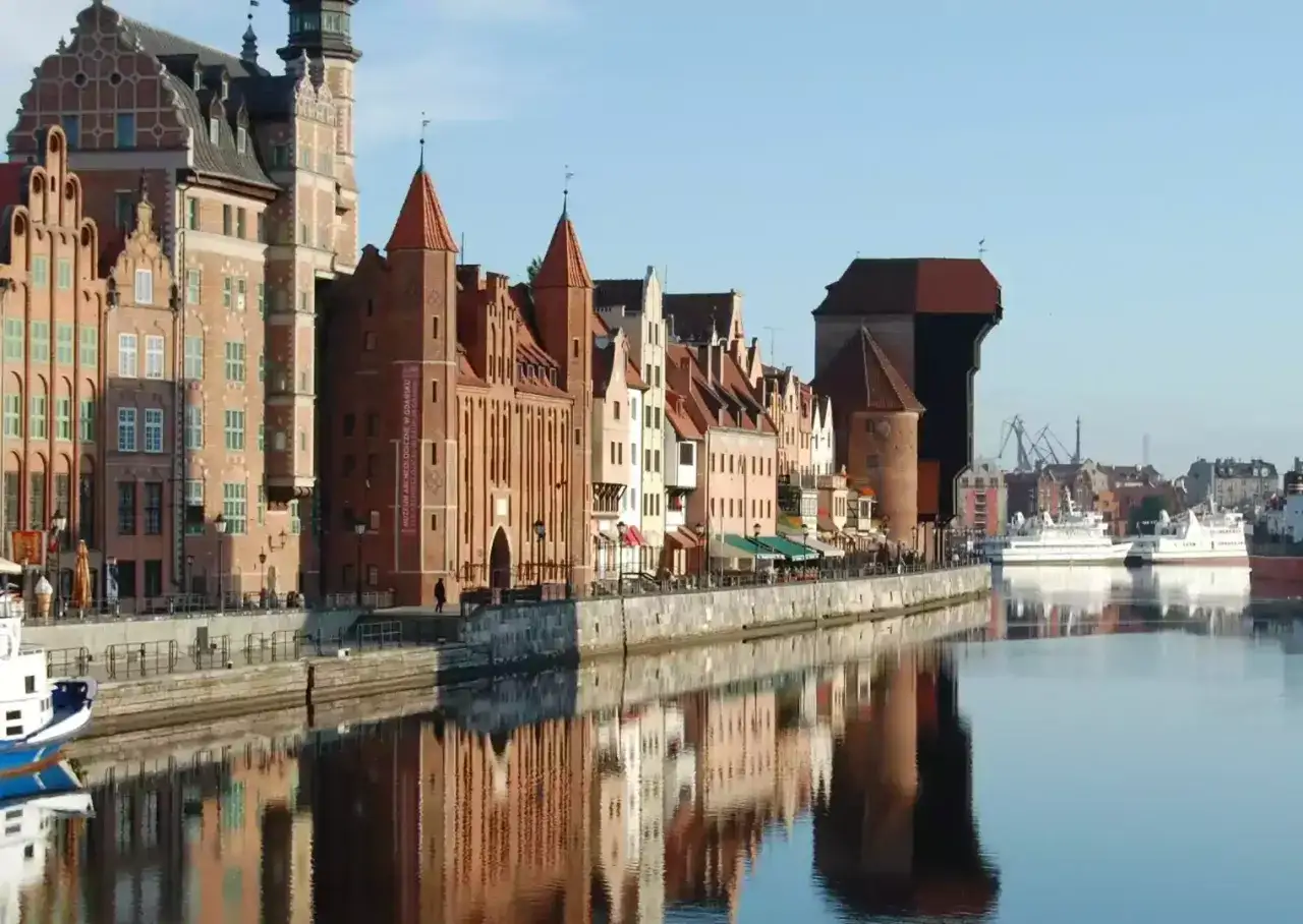 Zabytkowa gdańsk architektura nad Motławą, z Żurawiem w tle. Odbicia budynk&oacute;w w spokojnej wodzie.