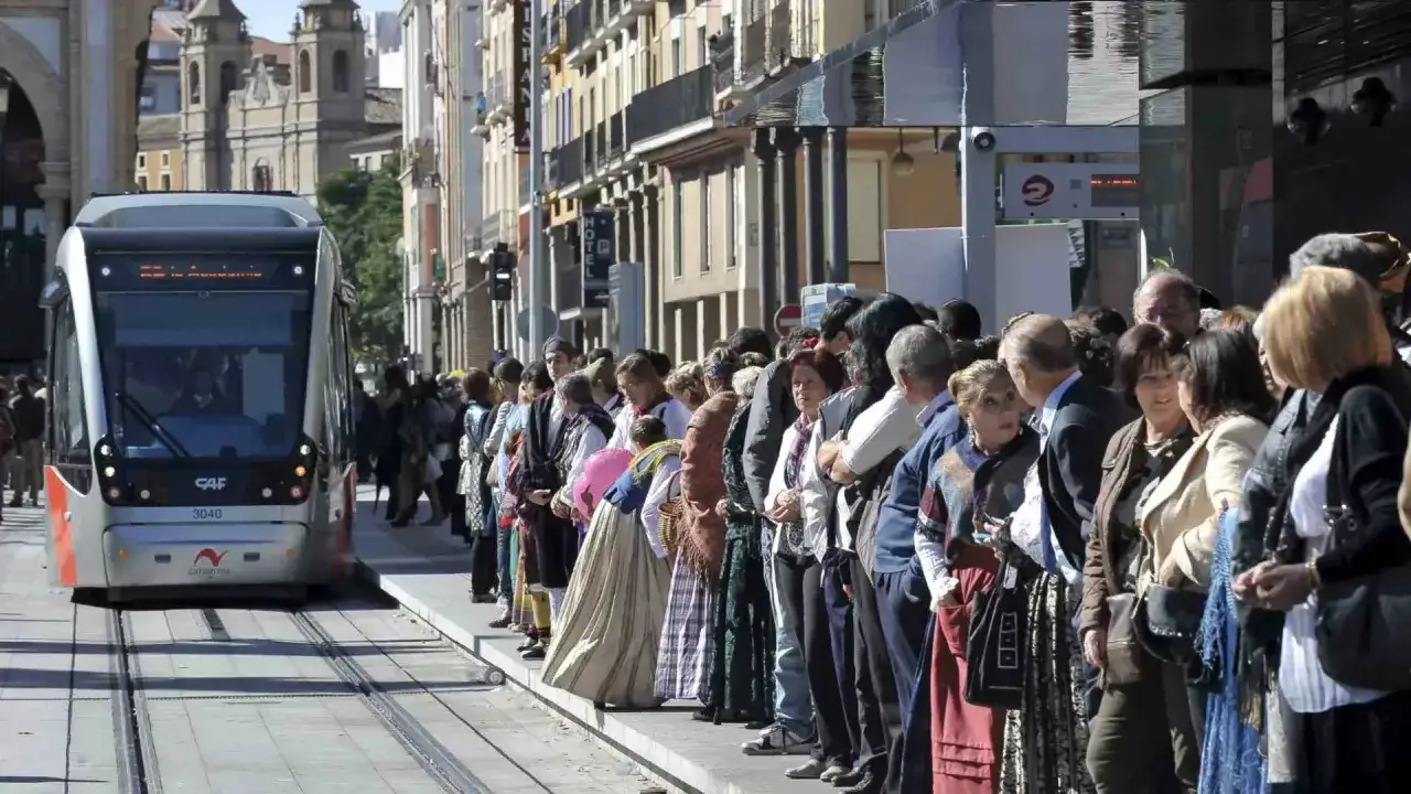 Línea de gente esperando el tranvía en un aforo espacio zity. El tranvía se acerca a la parada.