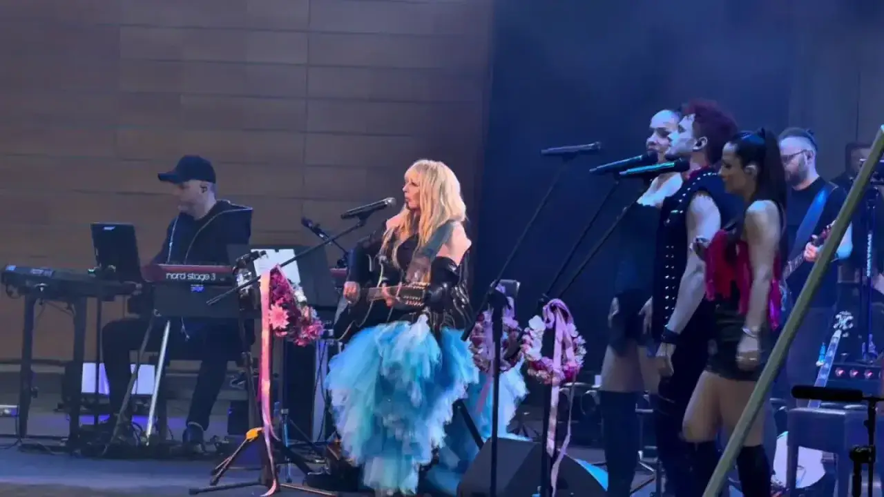 Maryla Rodowicz na scenie, w błękitnej, tiulowej sukni, gra na gitarze. Zespół towarzyszy jej w wykonaniu wszystkich przeboje Maryli Rodowicz.