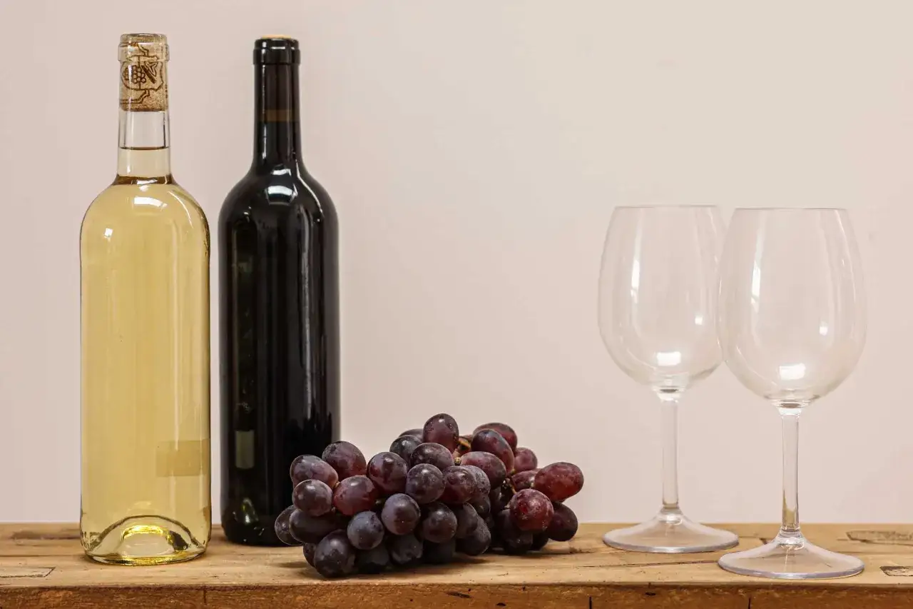 Zwei Flaschen Wein, eine helle und eine dunkle, mit einer Traube und zwei Gläsern. Perfekt für die **bester rotwein rangliste**.