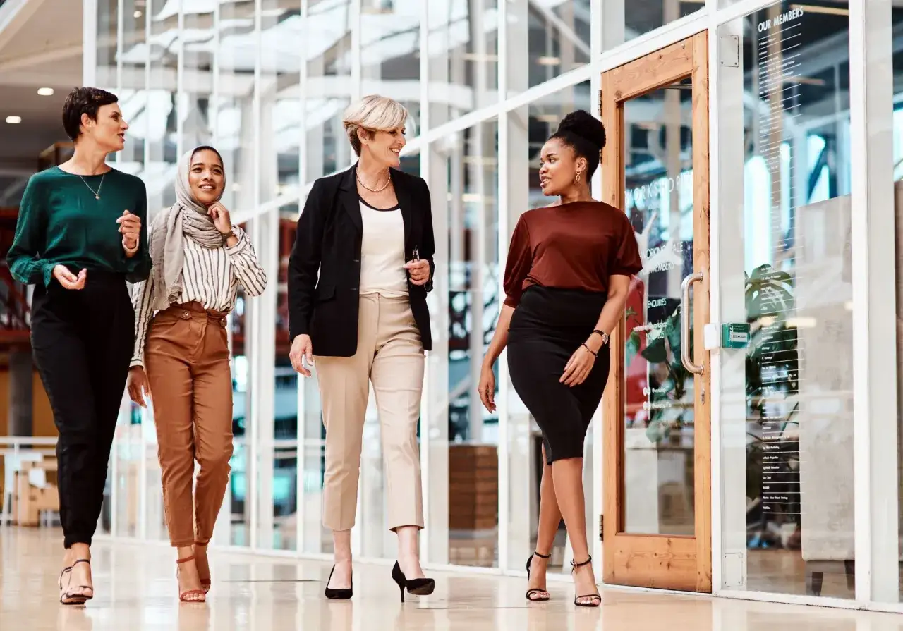Quatre femmes d'affaires discutent en marchant, chacune arborant une tenue pour réunion travail impeccable.