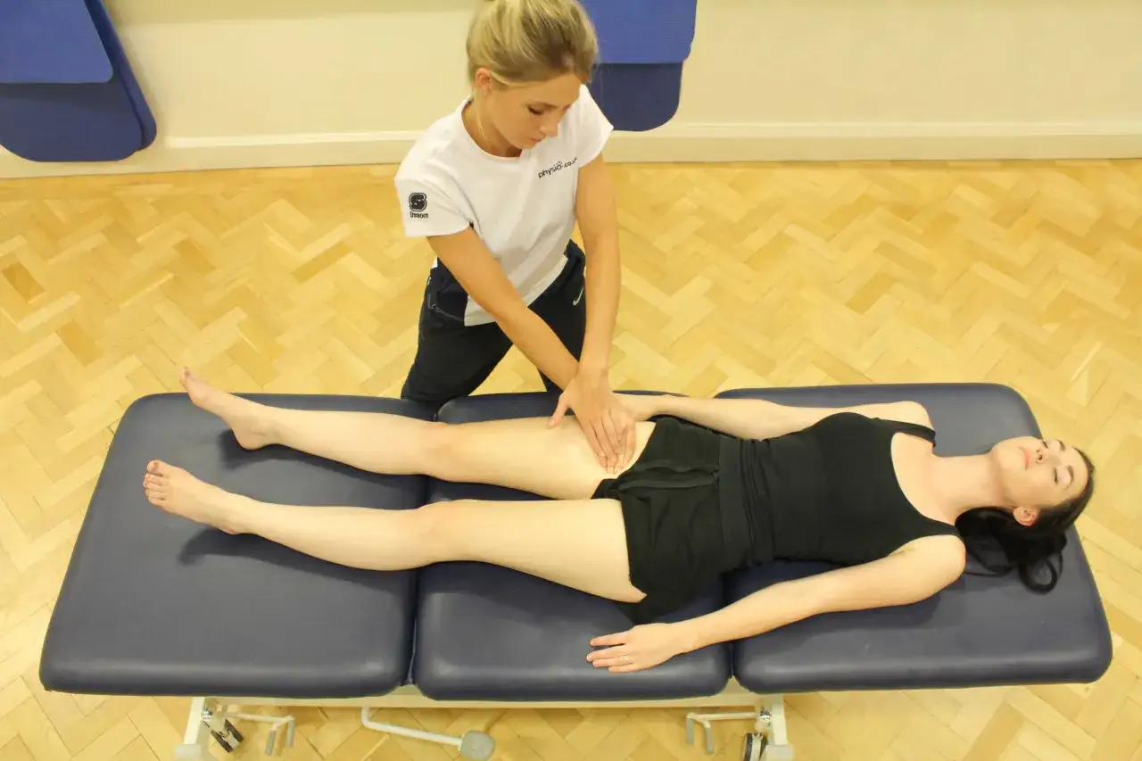 Fisioterapista massaggia il quadricipite femorale di una paziente sdraiata su un lettino.