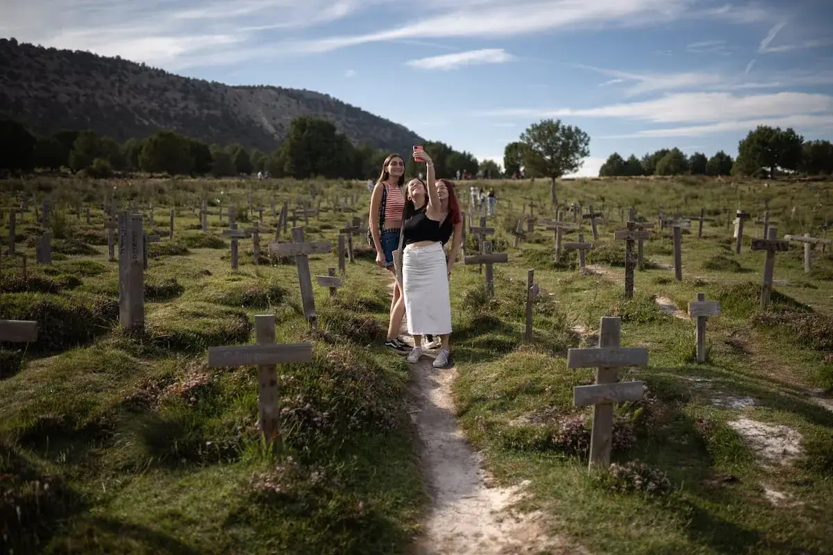 Tres j&oacute;venes toman una selfie en un **cementerio sad hill** con cruces de madera dispersas por la ladera.