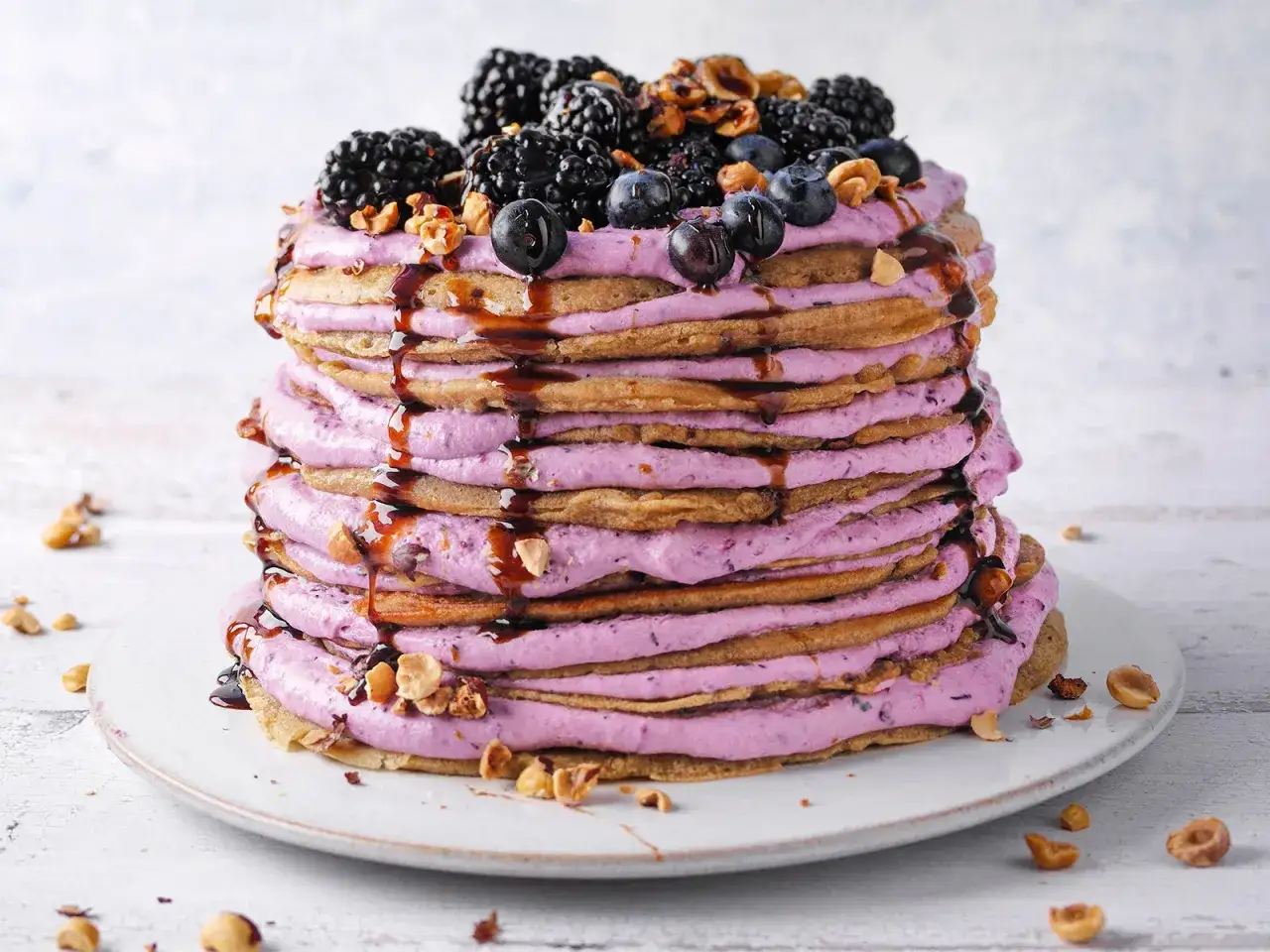 Eine beeindruckende Pfannkuchen Torte mit lila Creme, Beeren und N&uuml;ssen, betr&auml;ufelt mit dunkler Sauce.