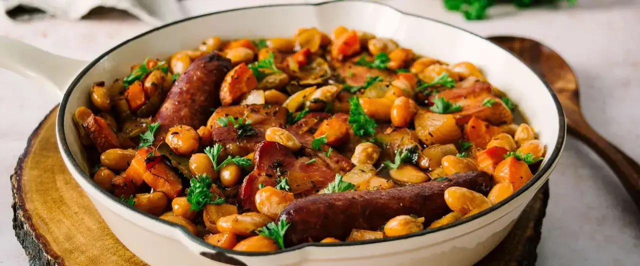 Herzhaftes Cassoulet-Rezept in einer Pfanne: wei&szlig;e Bohnen, Karotten, Speck und W&uuml;rstchen, garniert mit Petersilie.