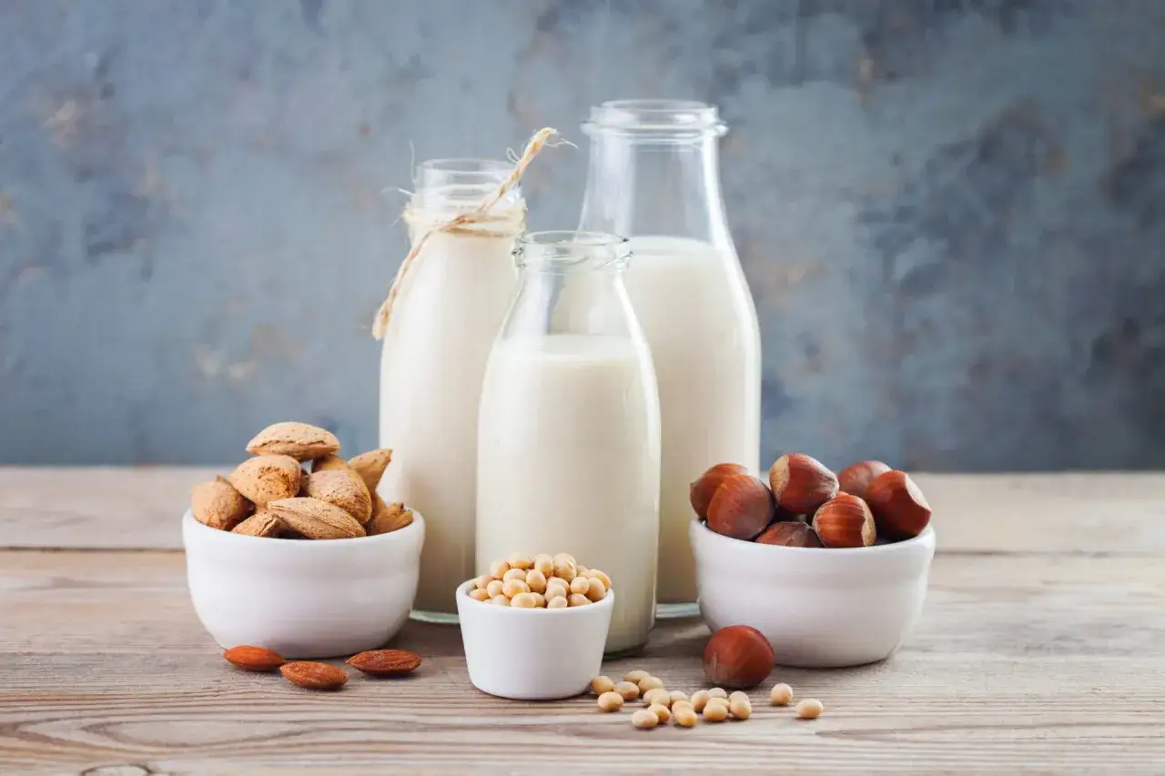 Trois bouteilles de lait v&eacute;g&eacute;tal, avec des amandes, des noisettes et des f&egrave;ves de soja dans des bols.