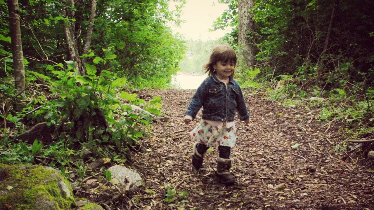 Glad liten flicka springer p&aring; en skogsstig. Perfekt f&ouml;r aktiviteter i skogen med barn.